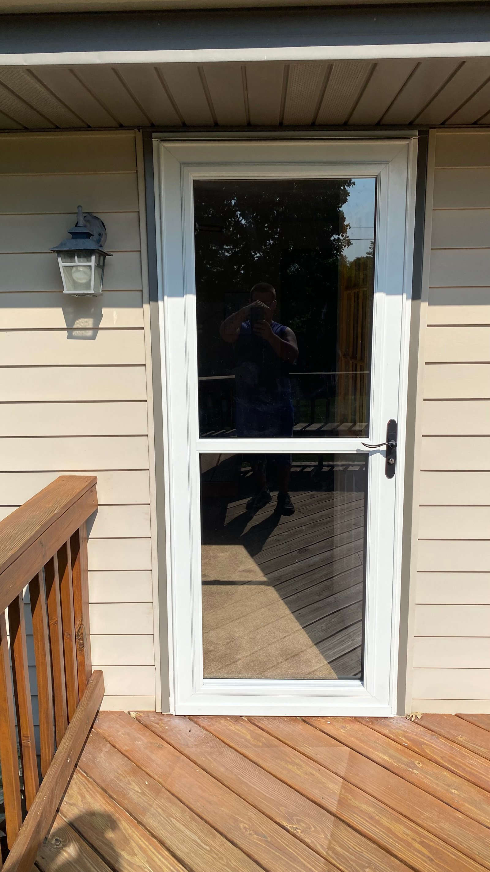 After: new white storm door with full glass and black handle, deck and entry light visible