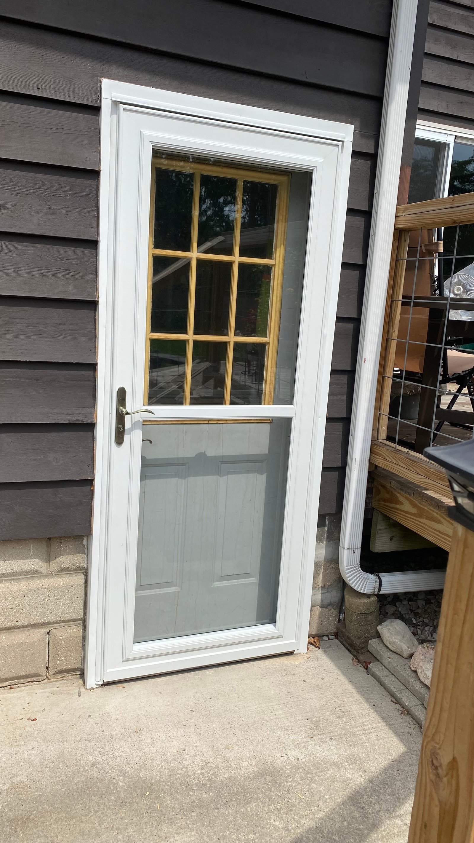 White storm door with divided glass and screen installed on dark siding