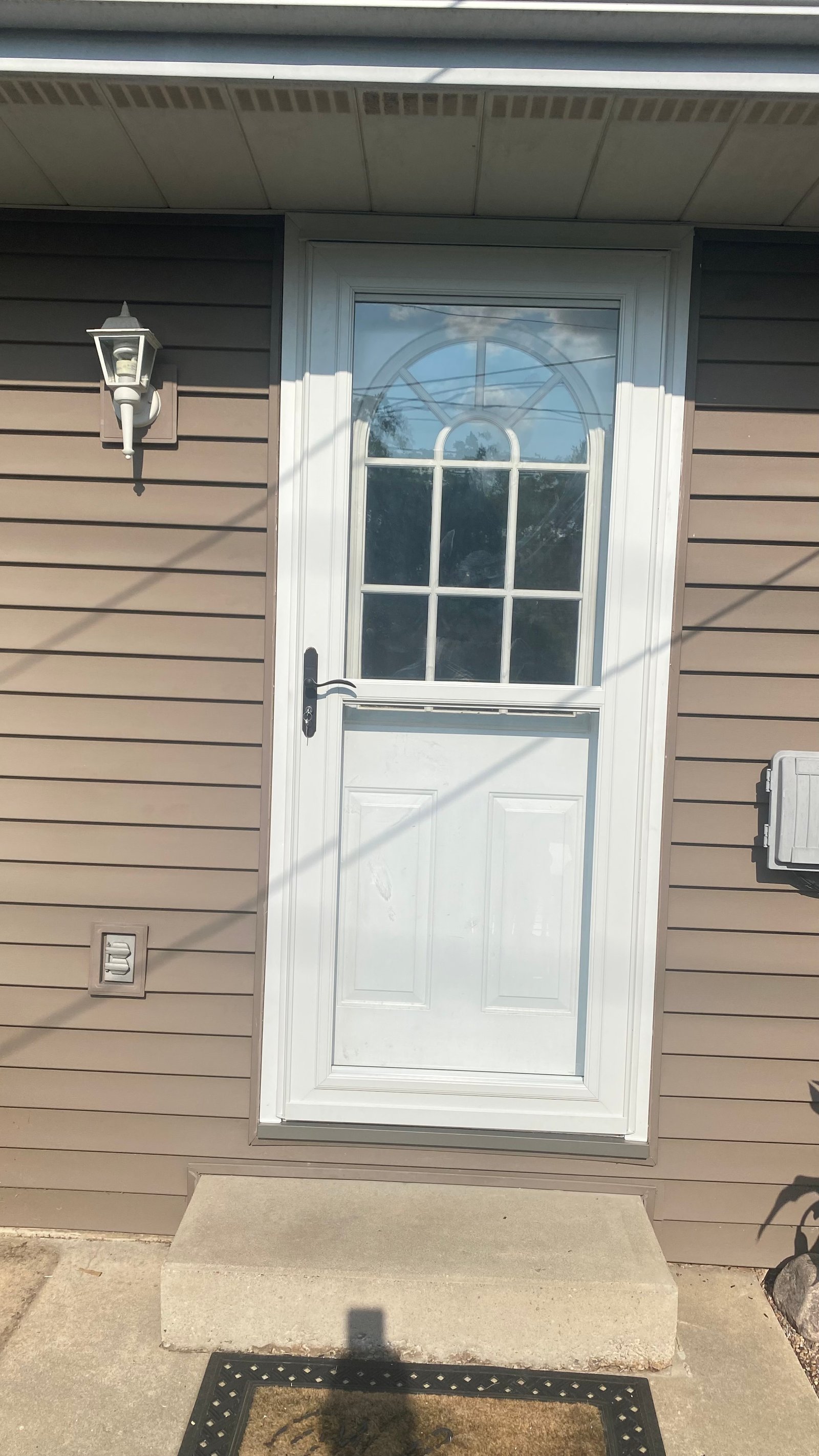 After: white storm door installed over the white entry door with arched window, full glass top with black handle